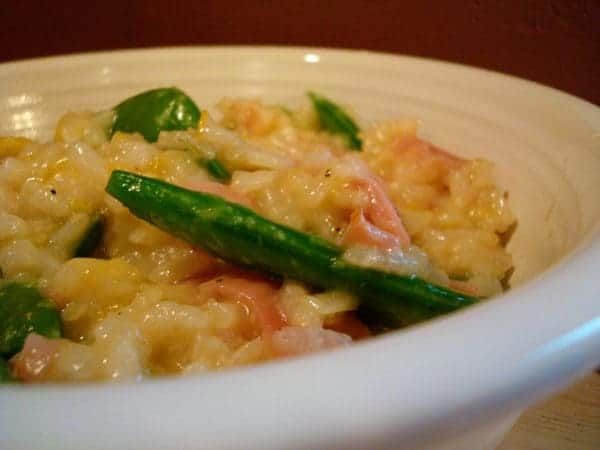 White bowl of risotto, sugar snap peas, and ham.