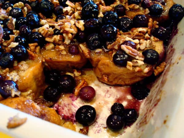 White dish with baked french toast and blueberries with a piece taken out.