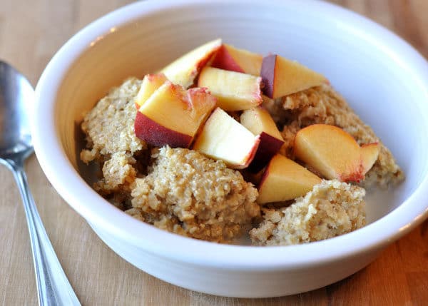 White bowl of oatmeal with fresh peach cut up on top.