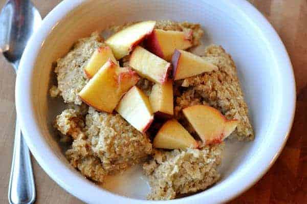 White bowl of baked oatmeal, milk, and fresh peach chunks.