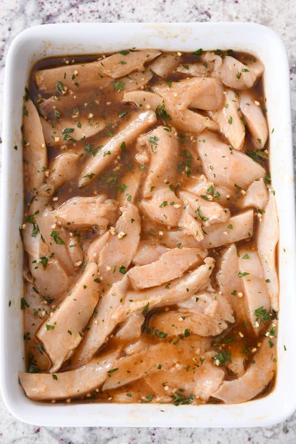 Chicken strips marinating in white dish.