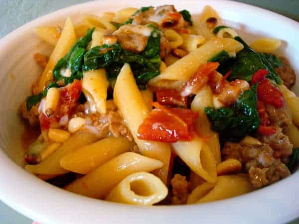 White bowl of pasta, wilted spinach, and tomatoes.