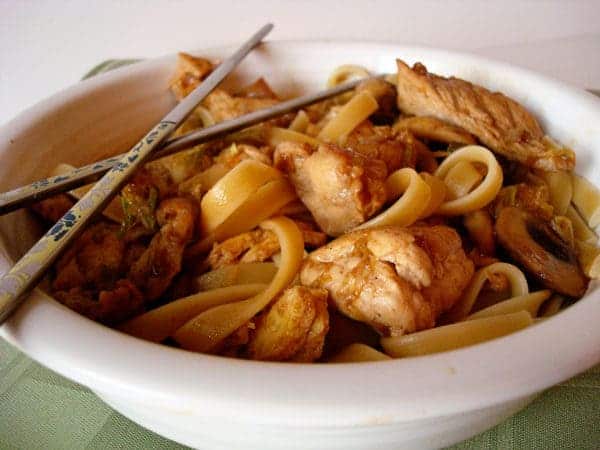 White bowl full of fettuccine noodles and chicken pieces.