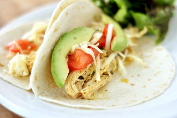 Two chicken tacos with avocado slices and tomatoes.