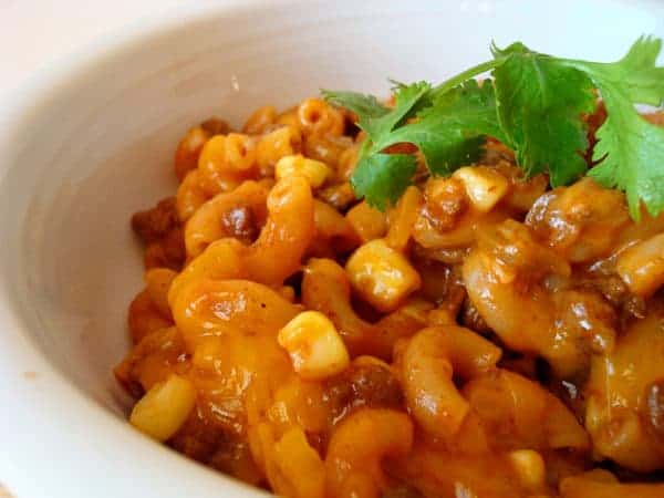 Chili pasta with corn and cilantro in a white bowl.