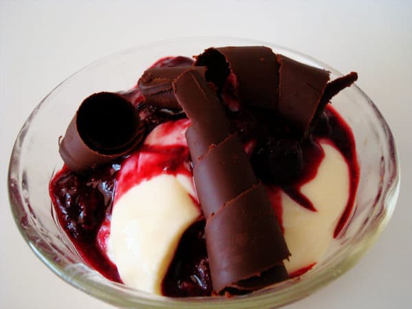 Glass bowl filled with cream, chocolate curls, and a berry sauce.
