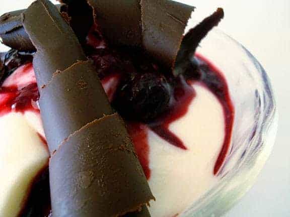 Glass bowl with cream, berry sauce, and a chocolate curl.