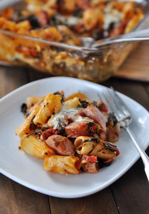 Baked pasta, cheese, chicken sausage, and a fork on a white plate.