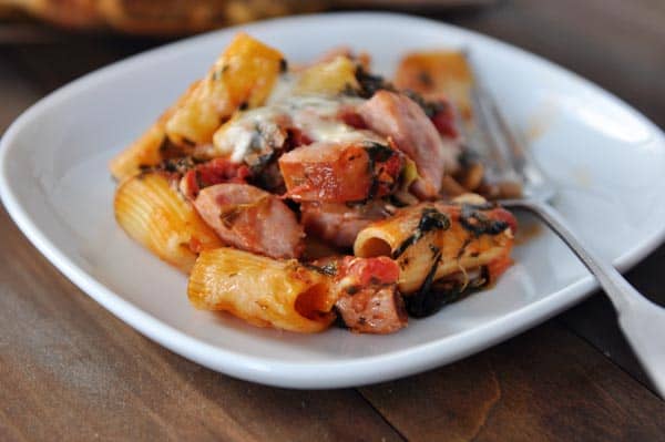 White plate with cooked tube pasta, slices of chicken sausage, and melted cheese.