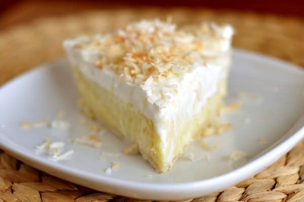 Slice of coconut cream pie on white plate.