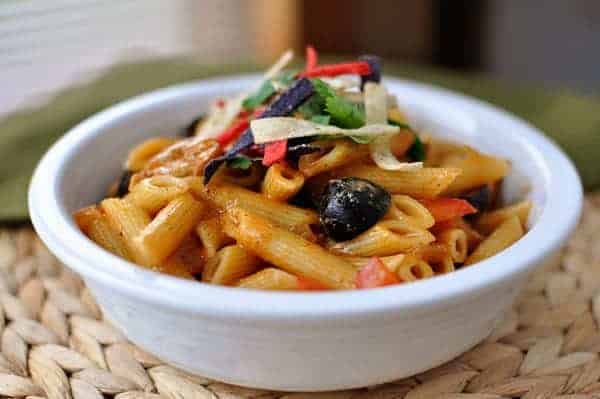 Tube pasta topped with olives and tortilla strips in a white bowl.