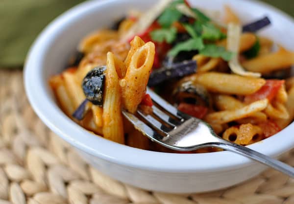 Fork with a bite of saucy pasta in a white bowl.