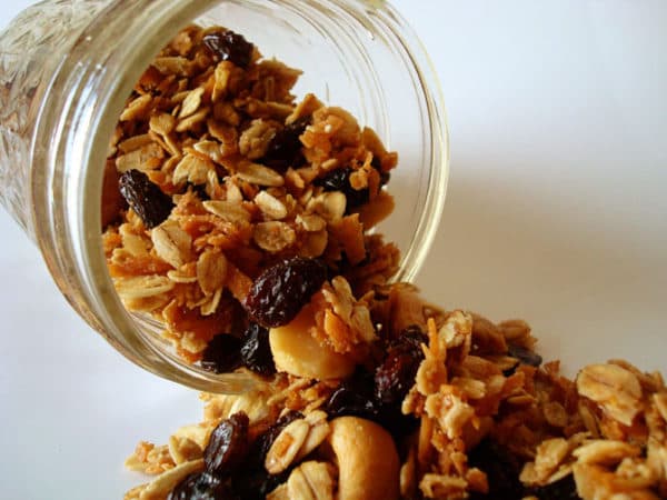 Cashew and raisin granola pouring out of a glass mason jar.