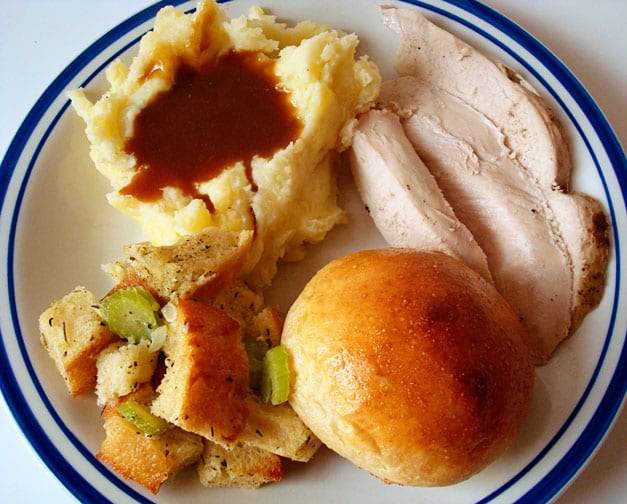 plate full of Thanksgiving stuffing, mashed potatoes and gravy, turkey, and a roll