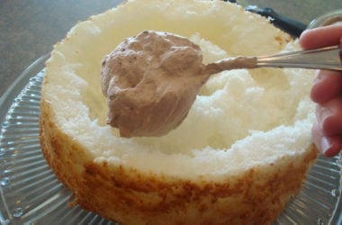 cut open angel food cake with chocolate frosting going in the middle