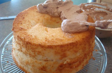 baked angel food cake with chocolate frosting starting to frost it