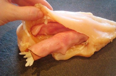 raw chicken breast cut open and getting stuffed with ham and cheese