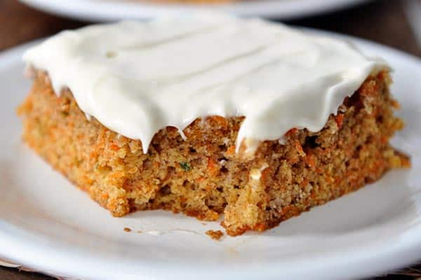 A piece of frosted carrot cake with a bite taken out on a white plate.