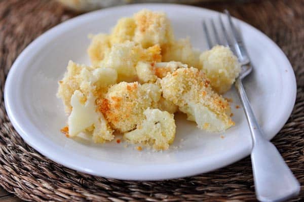 White plate with cheesy cooked cauliflower and a fork on the side.