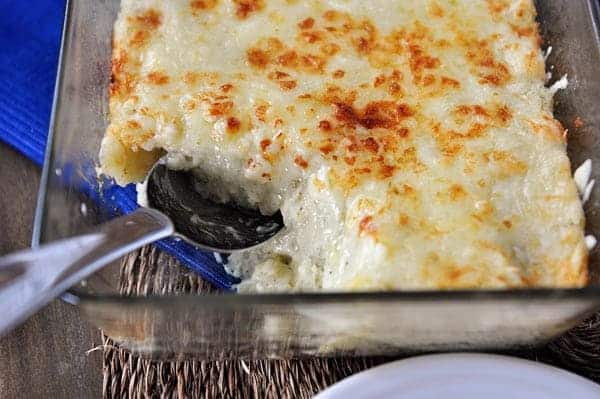 Casserole dish full of creamy, cheesy potatoes with a scoop taken out.