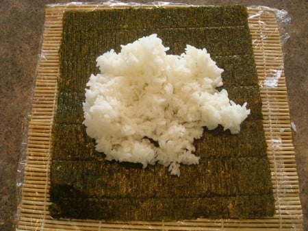 bamboo mat with sheet of nori and white rice on top