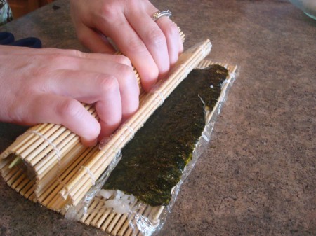 someone rolling a bamboo mat with a california sushi roll inside