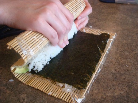 bamboo mat pressing down white rice on a sheet of nori