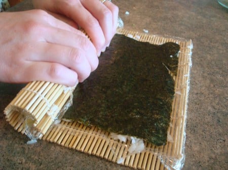 california sushi roll being rolled up with a bamboo mat