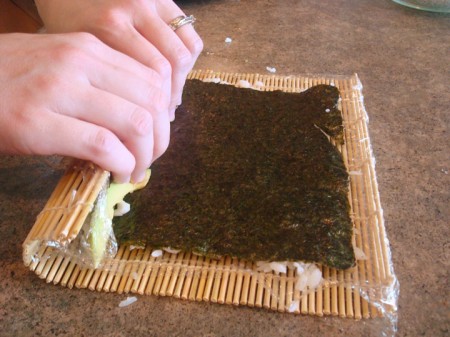 sushi roll being rolled up on a bamboo mat