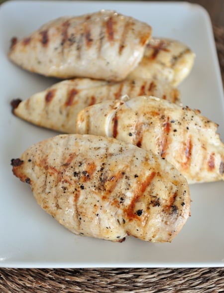 White platter with grilled chicken breasts lined up on it.