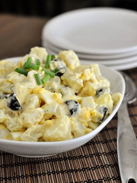 White bowl full of classic potato salad with sliced olives and topped with chives.