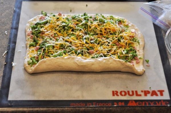 bread dough covered with toppings starting to be rolled into a log