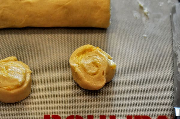 Uncooked filled orange rolls on a sheet pan.