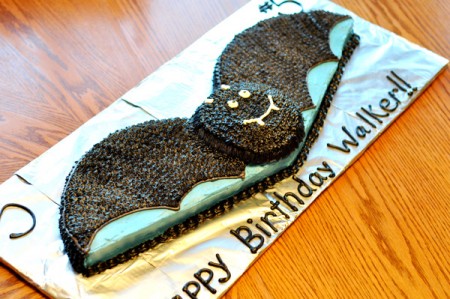 black bat cake on a tinfoil covered cake base with a happy birthday message written in frosting