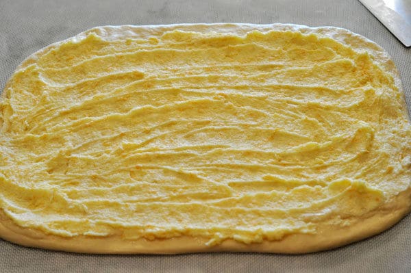 Rectangle shaped uncooked bread dough with orange zest and butter mixture spread on top.