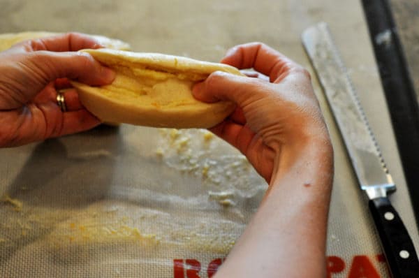 Hands stretching an uncooked sweet roll into an oblong shape.