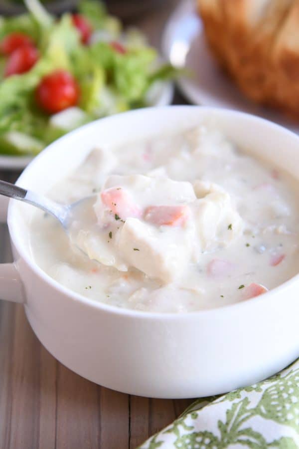 Scooping spoonful out of cream cheese chicken vegetable soup in white bowl.