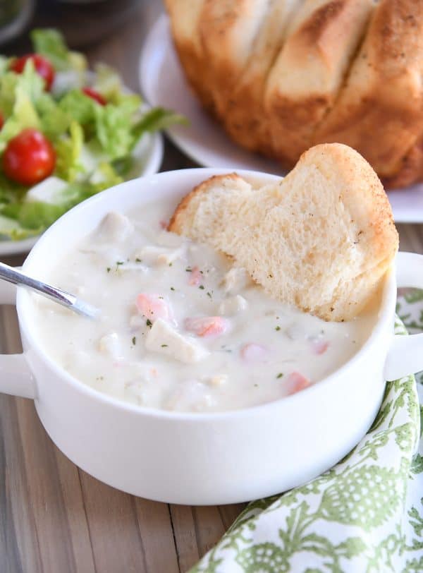 Cream cheese chicken vegetable soup with bread in white bowl.