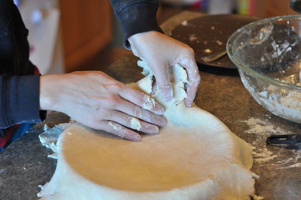 a pie crust being lifted into a pie dish