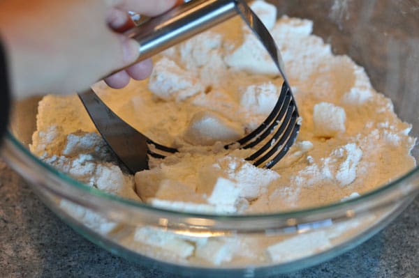 pastry blender blending cubed butter and flour in a glass bowl