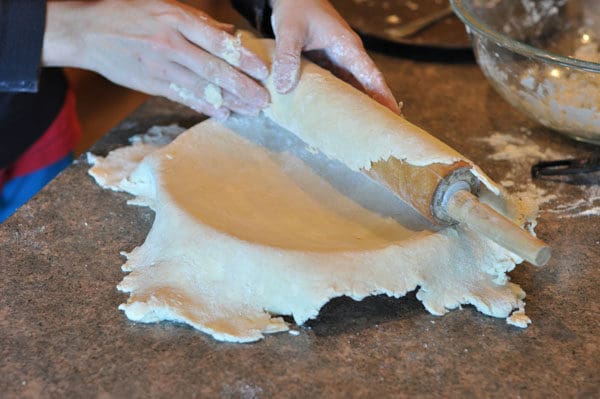 unrolling a pie crust over a pie dish