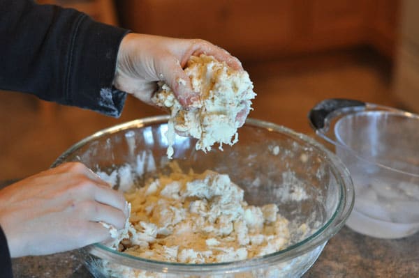 handful of dough over the top of a glass bowl of dough