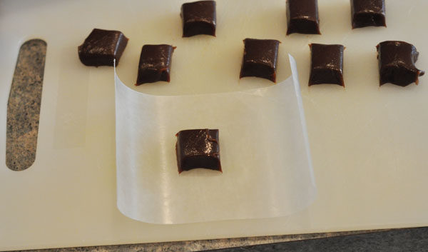 small squares of chocolate caramels on a white cutting and one on a piece of parchment