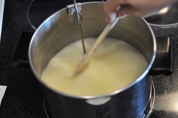 sugar mixture dissolving in a large pot with a wooden spoon and candy thermometer inside