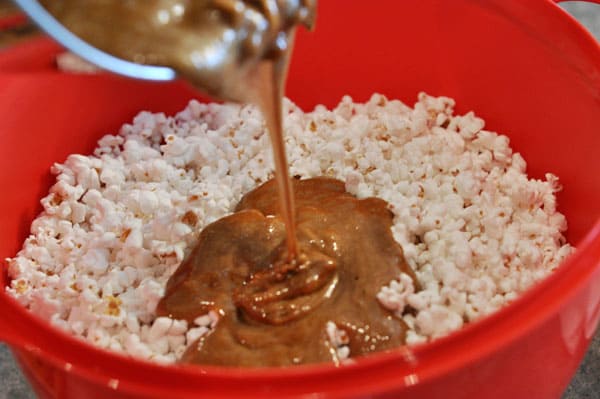 caramel mixture being poured over a red bowl of popped popcorn