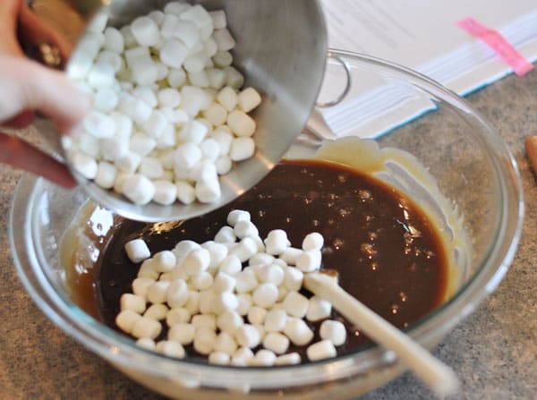 fudge mixture in a glass bowl with marshmallows being dumped in