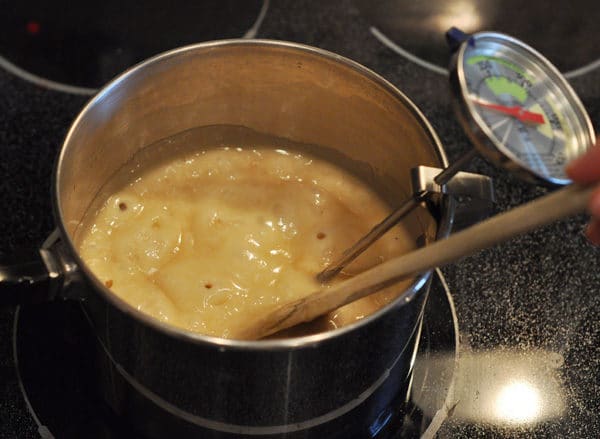 saucepan full of bubbling butter mixture with a wooden spoon and candy thermometer clipped to the side