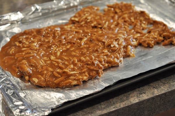 caramel and almonds mixture being spread on a tinfoil lined cookie sheet
