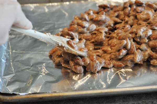 candy coated almonds being spread on a tinfoil lined cookie sheet