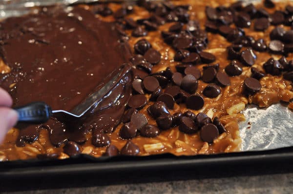 offset spatula spreading melted chocolate over chocolate chip covered almond roca